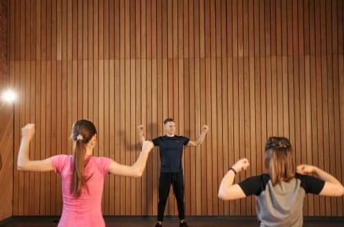 Instructor guiding two women in a gym workout session. Indoor fitness training.